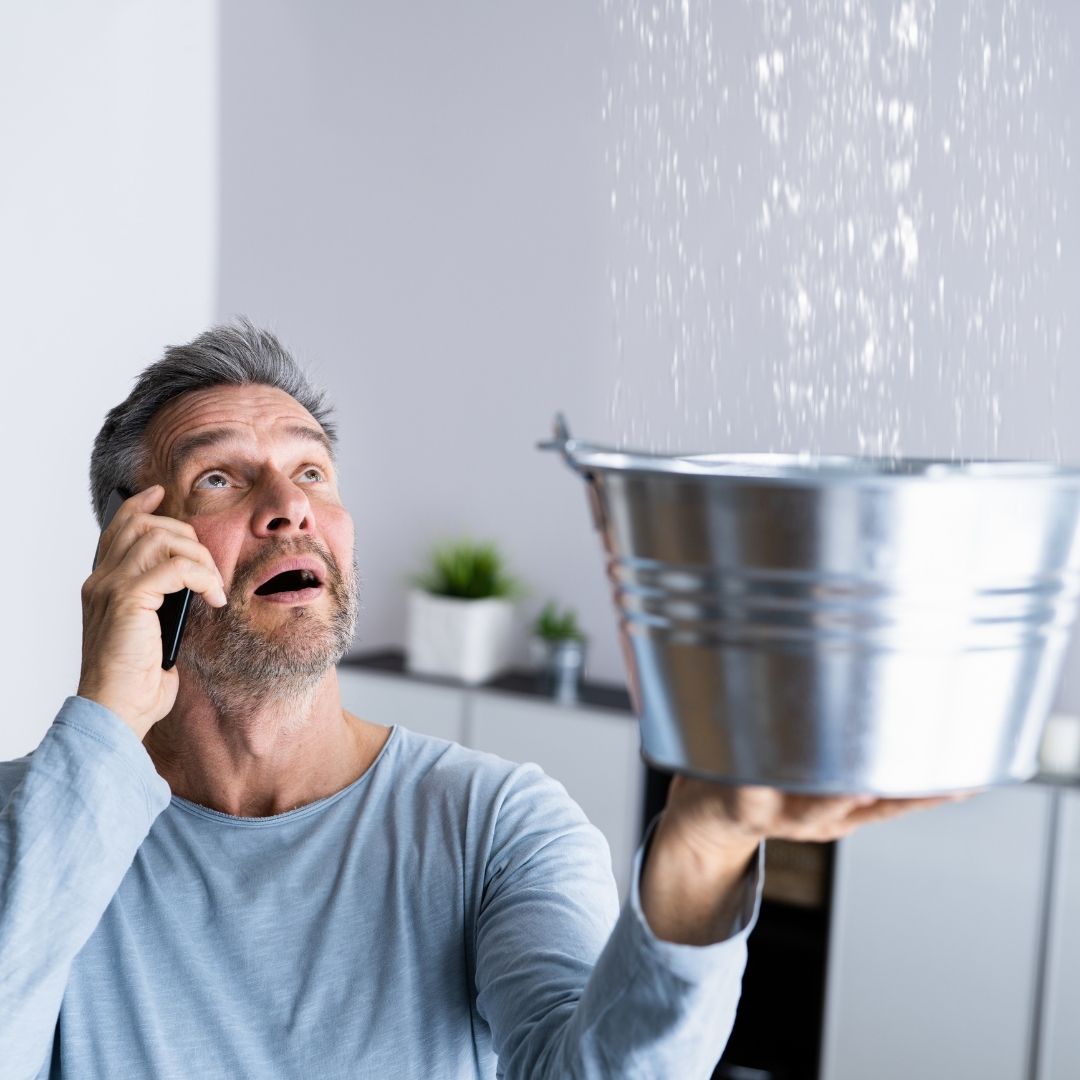 older-gentleman-on-phone-holding-bucket-collecting-water-leak