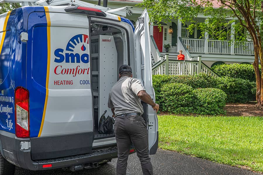 Smoak’s Comfort Control technician opening the back of a branded service van outside a home with a wraparound porch while the homeowner waits on the front steps